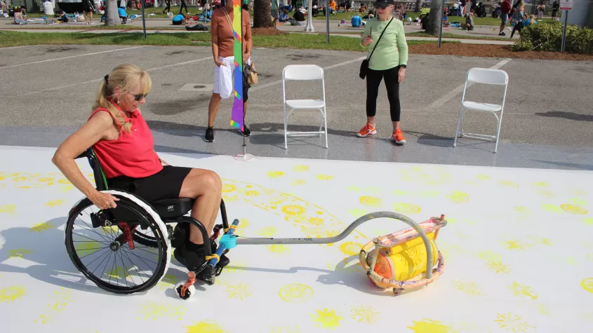 A wheelchair user participates in our "Art for All" activity, which allows disabled patrons as well as children participate in a large collaborative street painting.