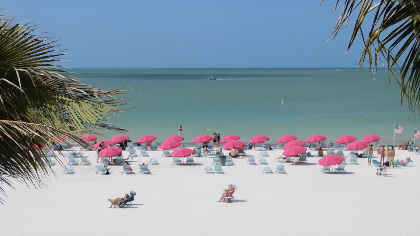 balcony view of white sandy beach, palm trees, pink umbrellas in the sand and blue water