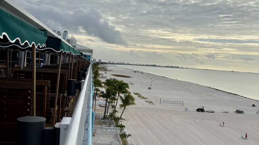 rooftop view overlooking the beach with white clouds, light sunset and palm trees and white sand