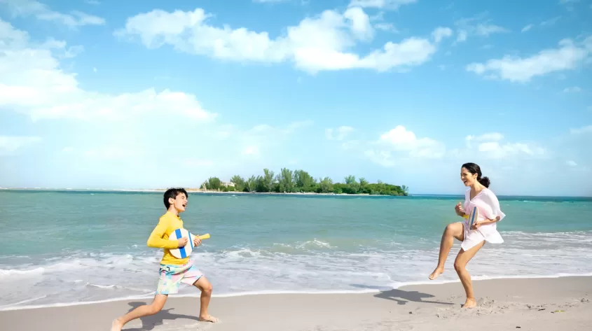 A mom and her son jump on the beach and pretend to play the guitar 