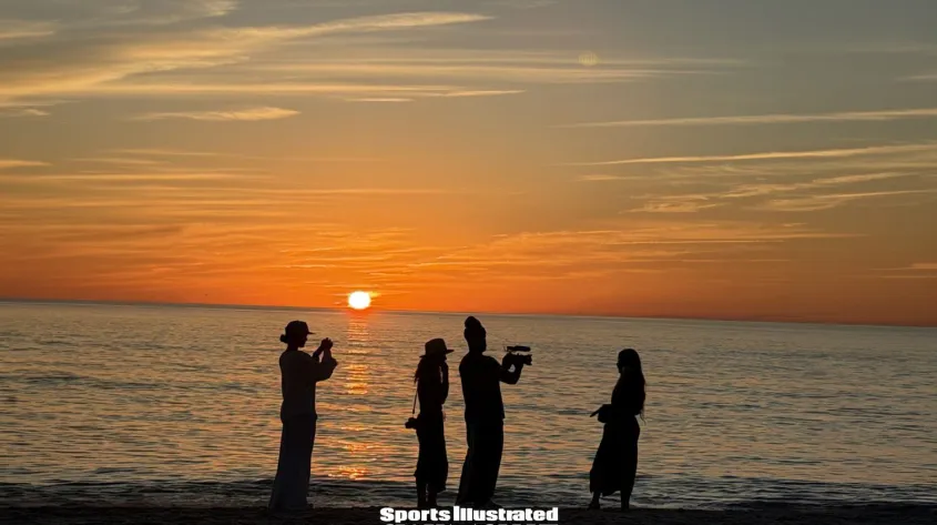 Silhouettes of four people standing on a beach at sunset with text reading “Fort Myers Through the Lens of SI Swimsuit.”