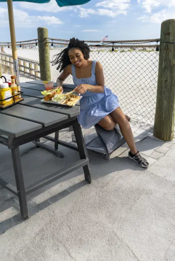 Woman enjoying a meal at an outdoor picnic table beside a sandy beach in Fort Myers.