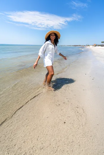 Woman in a straw hat walking through shallow water on a Sanibel Island beach