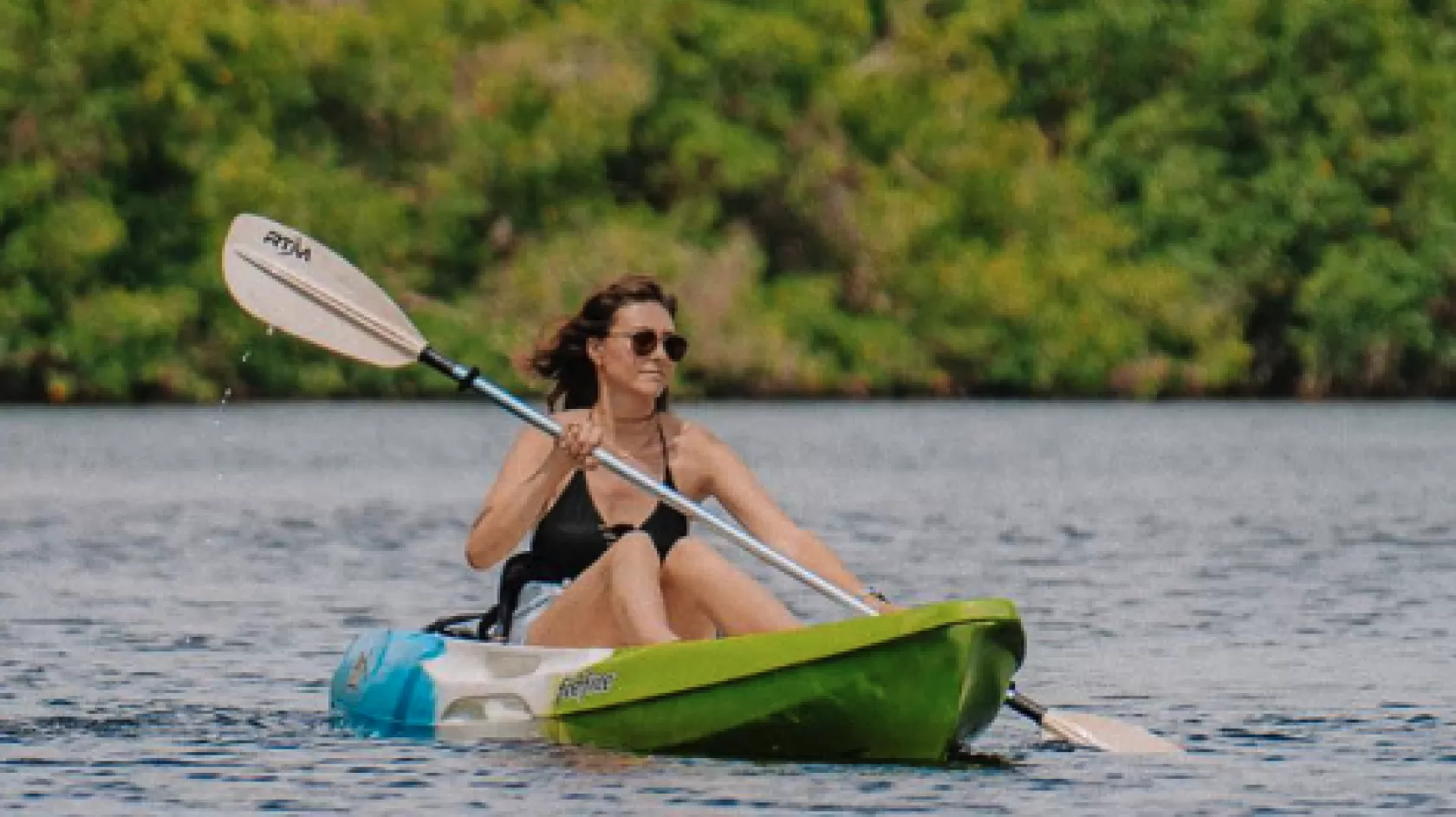 A woman paddles through calm waters on a kayak