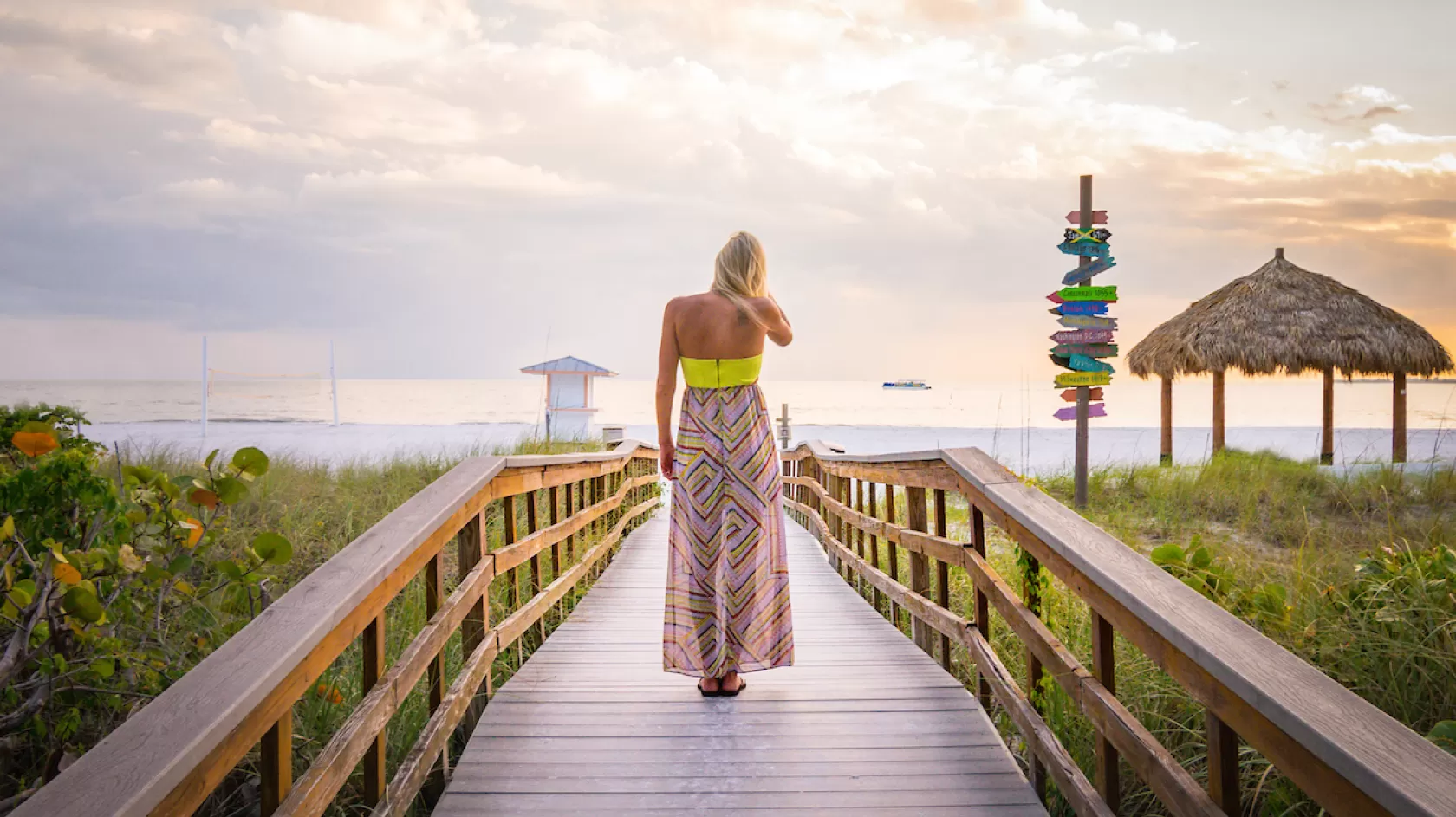 A woman walks towards the beach on a boardwalk overpass