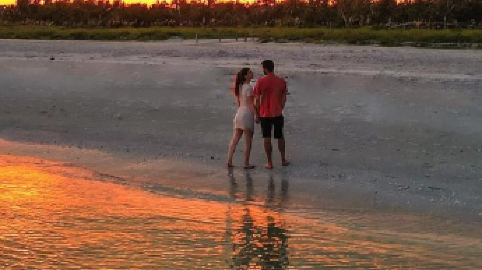 A man and a woman pose on the beach at sunset