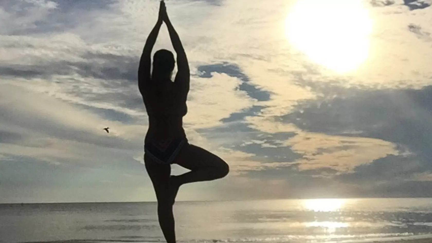 A woman on the beach does yoga at sunset