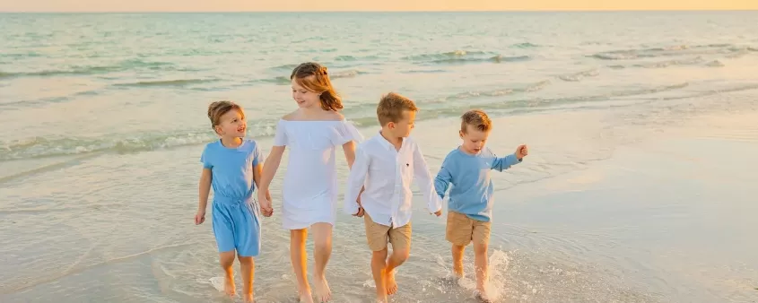 Four kids walking hand in hand on shoreline of sanibel island at sunset