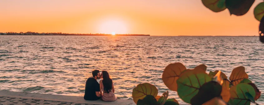A couple kisses as the sun sets over the water