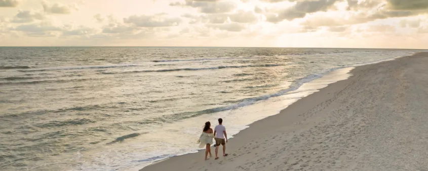 A couple walks along a secluded beach at sunset