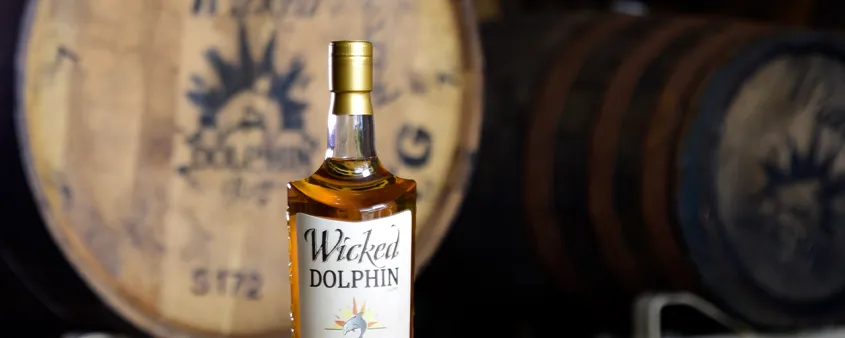 Wicked Dolphin rum bottle and cocktail on a barrel.