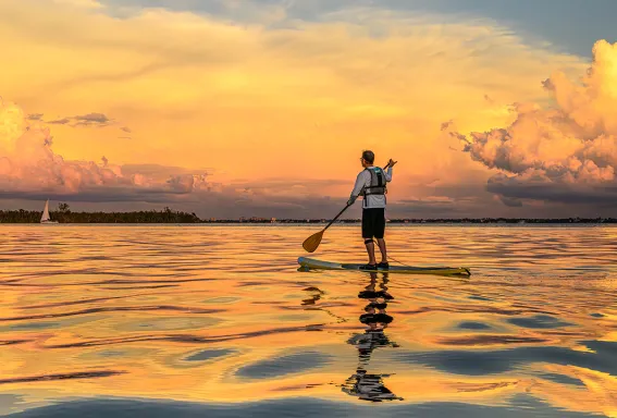 Paddleboarder on golden water at sunset.