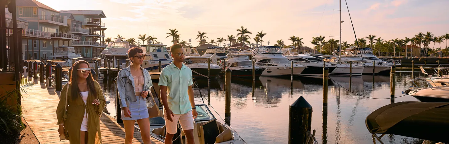 People walk along a marina dock at sunset.