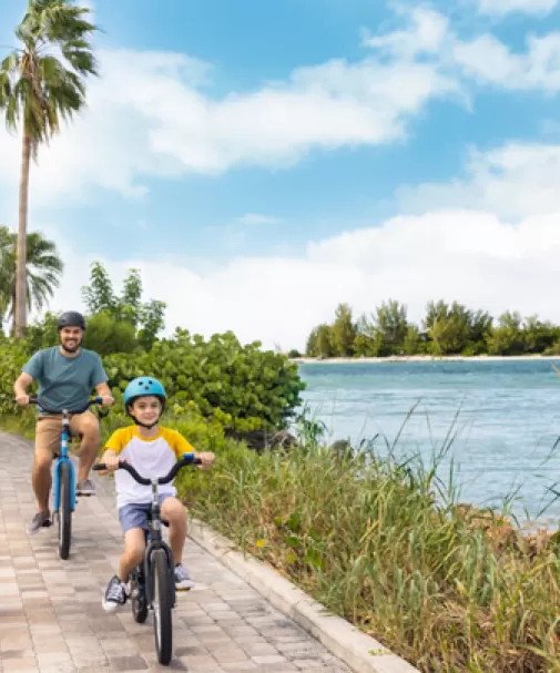 A dad and his son ride bikes alongside the water