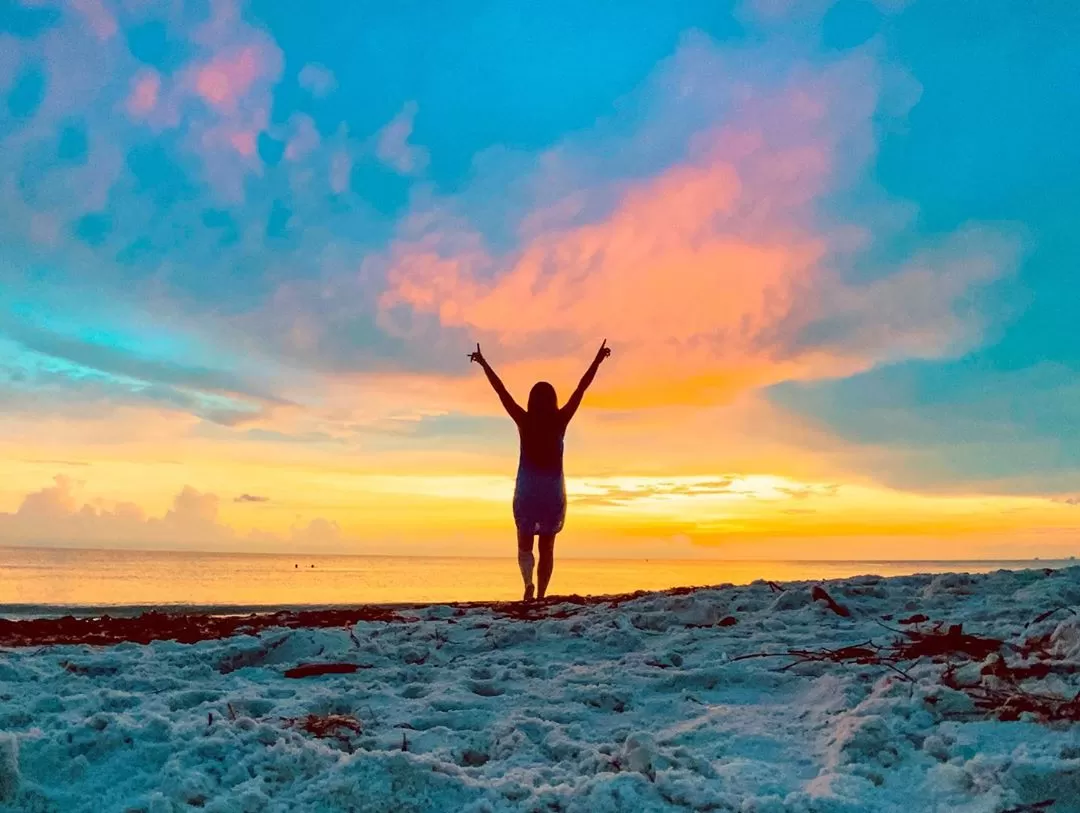 woman standing on beach with arms in the air