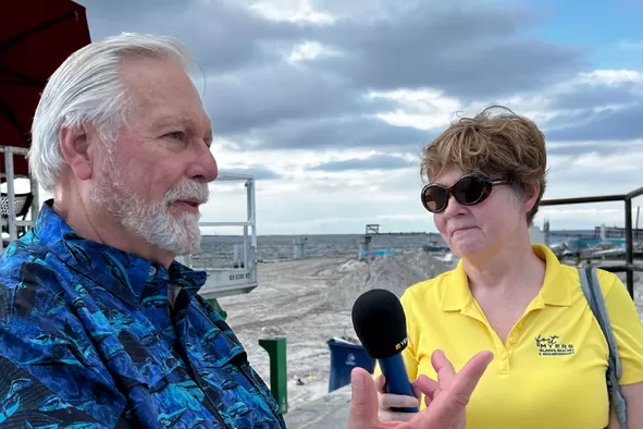 a man and a woman stand as they record a podcast episode on fort myers beach